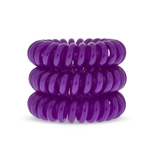 A tower of 3 purple berry coloured hair bobbles called spirabobbles. A beige plastic spiral circular hair tie spira bobble.