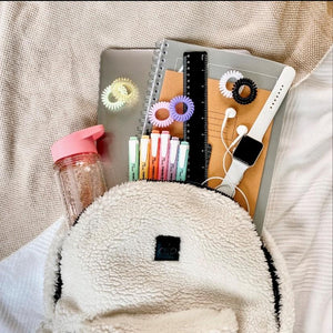 Fluffy rucksack with school contents showing including different coloured spirabobbles and a waterbottle and a laptop