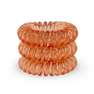 A tower of 3 orange segment coloured hair bobbles called spirabobbles. A plastic spiral circular hair tie spira bobble.