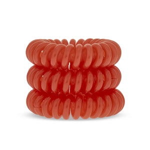 A tower of 3 bright oramge coloured hair bobbles called spirabobbles. A plastic spiral circular hair tie spira bobble.