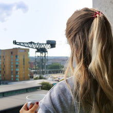 Load image into Gallery viewer, Girl with her hair up in spirabobble with a mug of coffee
