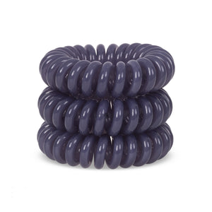 A grey solid coloured plastic circular hairband on a white background that looks like an old fashioned curly coiled telephone cable or a coiled spring which has been made into a circular shape